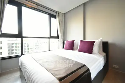 Modern bedroom with large window and stylish decor in urban apartment.