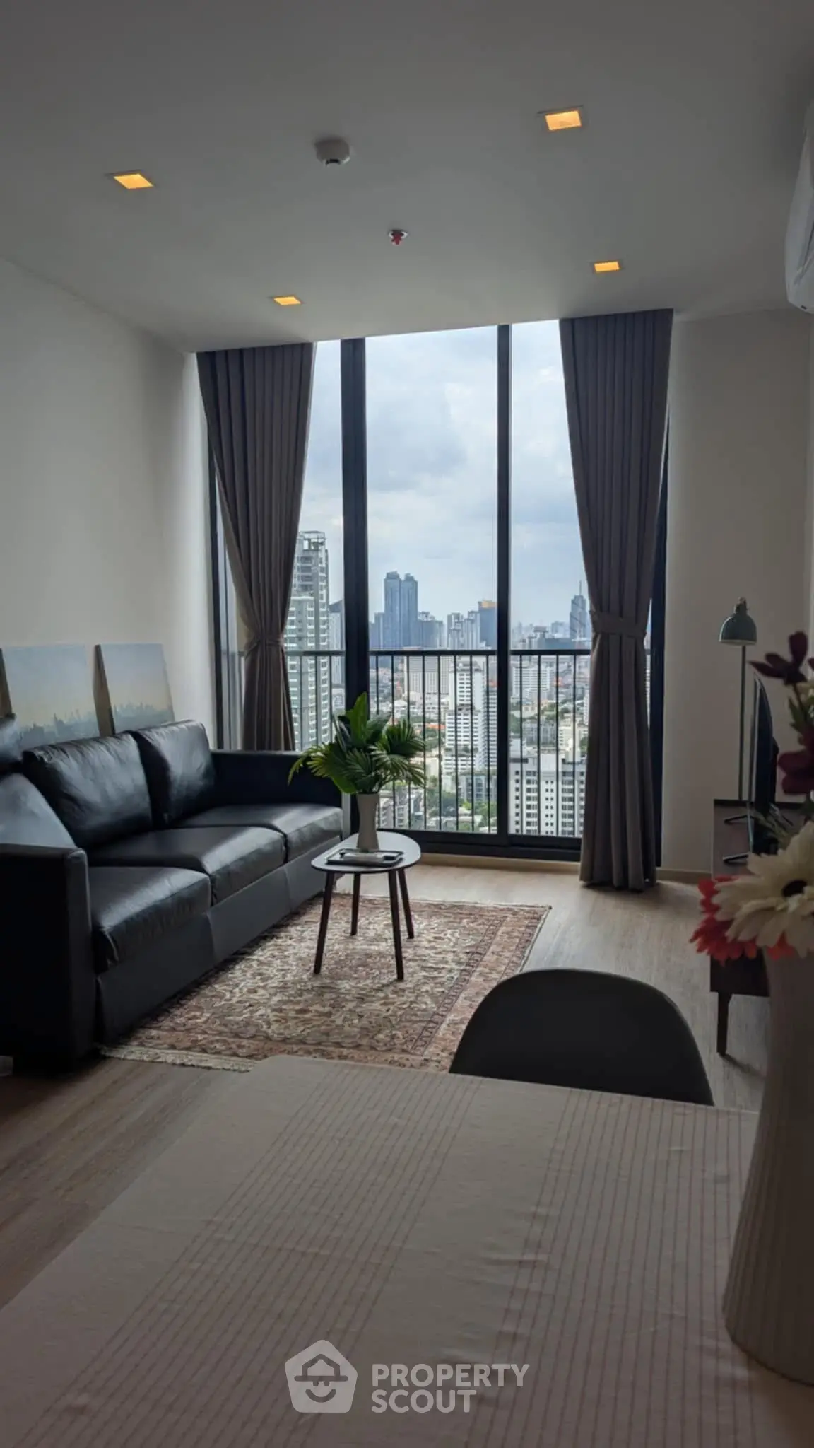 Modern living room with city view, featuring sleek furniture and floor-to-ceiling windows.