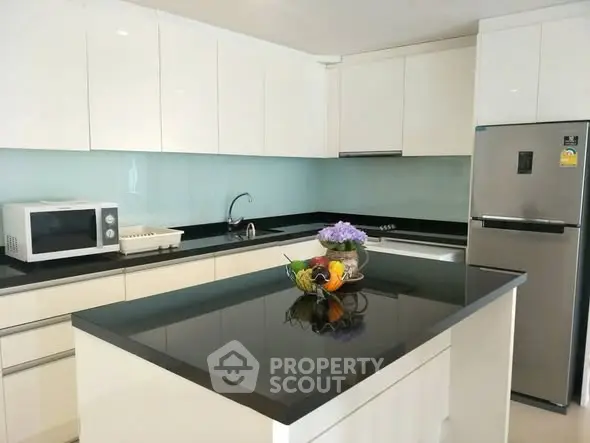 Modern kitchen with sleek white cabinets and black countertops featuring a stainless steel fridge and microwave.