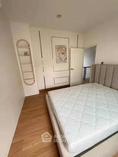 Spacious bedroom with elegant decor and hardwood flooring, featuring a comfortable bed and built-in shelving.
