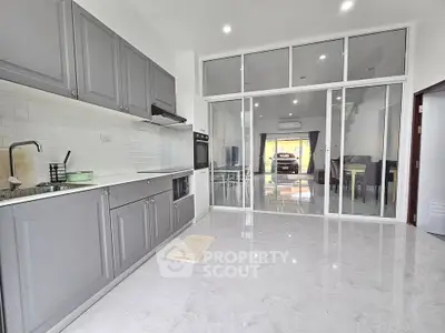 Modern kitchen with sleek gray cabinets and open layout, leading to a spacious living area.