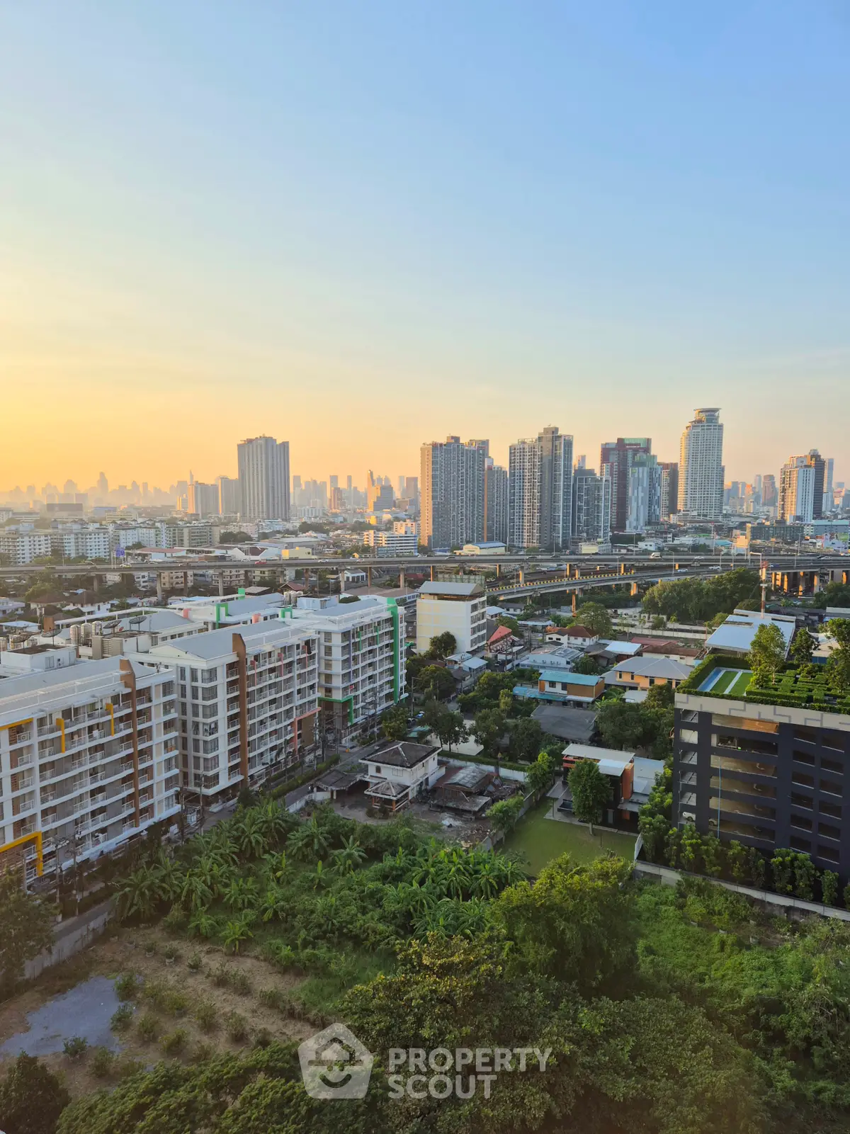 Stunning cityscape view from a high-rise apartment at sunset, showcasing urban skyline and lush greenery.