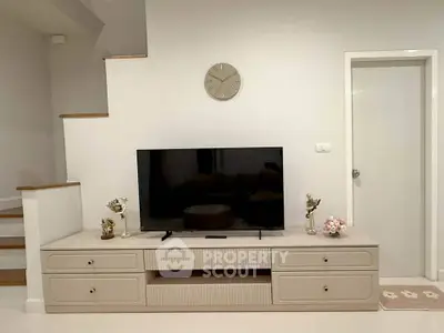 Modern living room with stylish TV stand and staircase, featuring elegant decor and neutral tones.