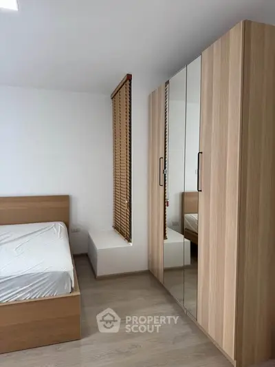 Modern bedroom with wooden furniture and mirrored wardrobe in a bright apartment.
