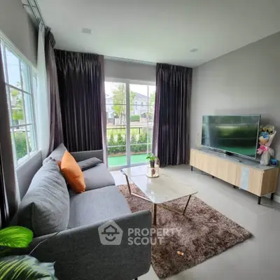 Stylish living room with modern sofa, TV, and garden view through large windows.