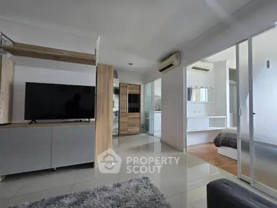 Modern open-plan living room with sleek furniture and large TV, adjacent to a cozy bedroom.