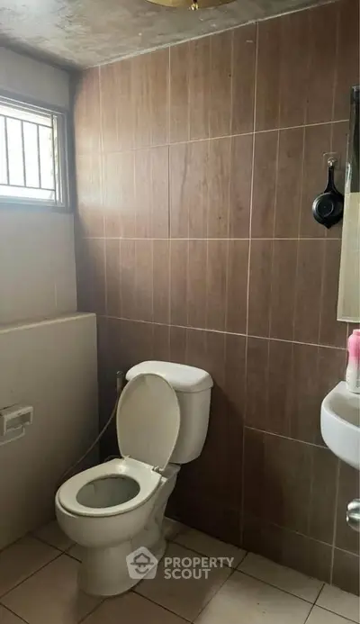 Compact bathroom with tiled walls and window, featuring a toilet and small sink.