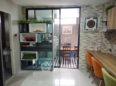 Modern open-plan kitchen with stylish decor and dining area, featuring vibrant chairs and sleek shelving.