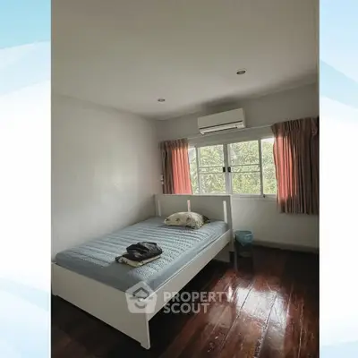 Cozy bedroom with wooden flooring and large window offering natural light.