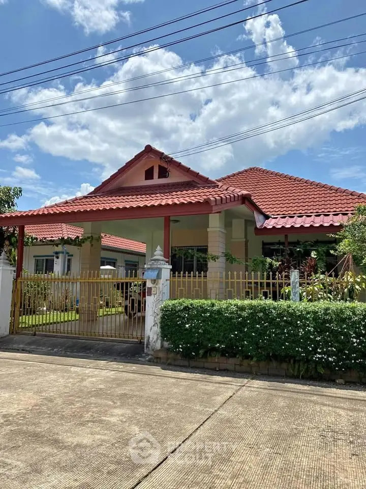 Charming single-story house with red roof and gated entrance under a clear blue sky.
