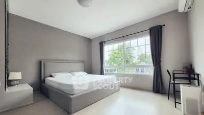 Spacious bedroom with large window and modern decor in a bright, airy setting.
