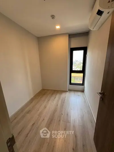 Spacious bedroom with wooden flooring and city view window in modern apartment.