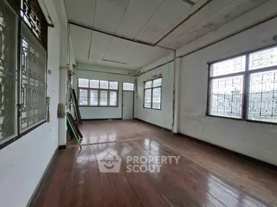 Spacious empty room with wooden floors and large windows offering natural light.