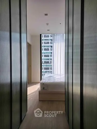 Modern bedroom with floor-to-ceiling windows and city view, featuring sleek design and natural light.