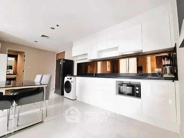 Modern kitchen with sleek white cabinets, built-in appliances, and dining area in a stylish apartment.