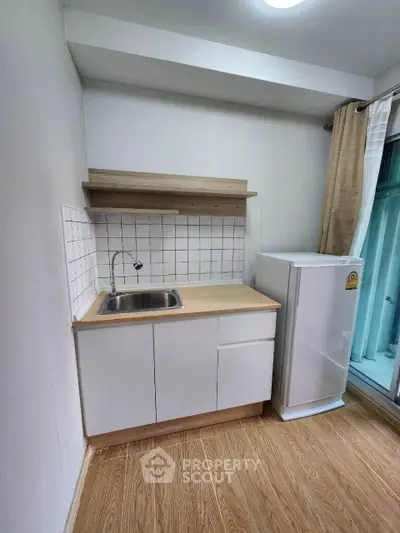 Compact kitchen with white cabinets and small fridge in modern apartment
