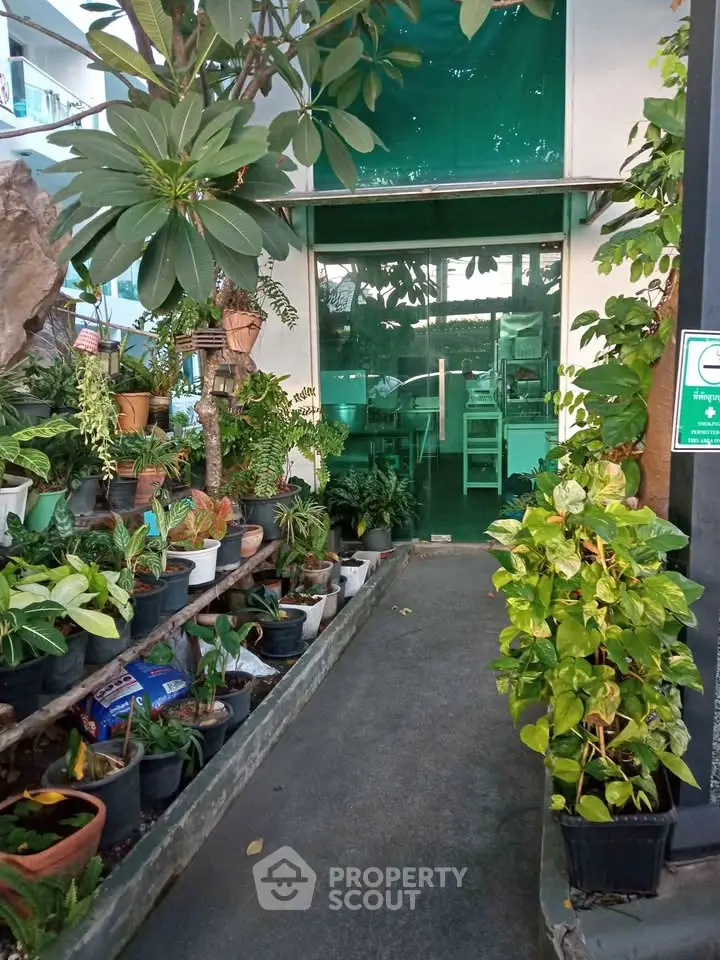 Charming entrance with lush greenery leading to a modern glass door, perfect for a serene workspace.