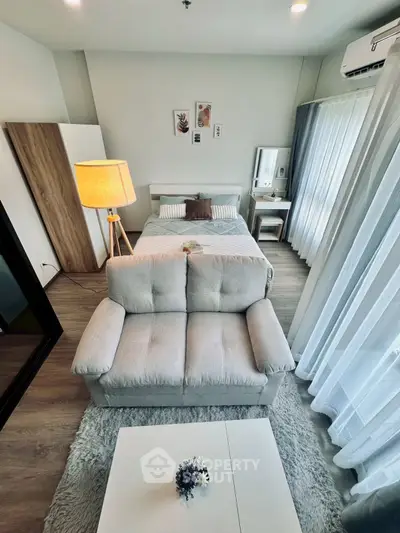Cozy bedroom with modern decor, featuring a plush sofa and natural light through large windows.