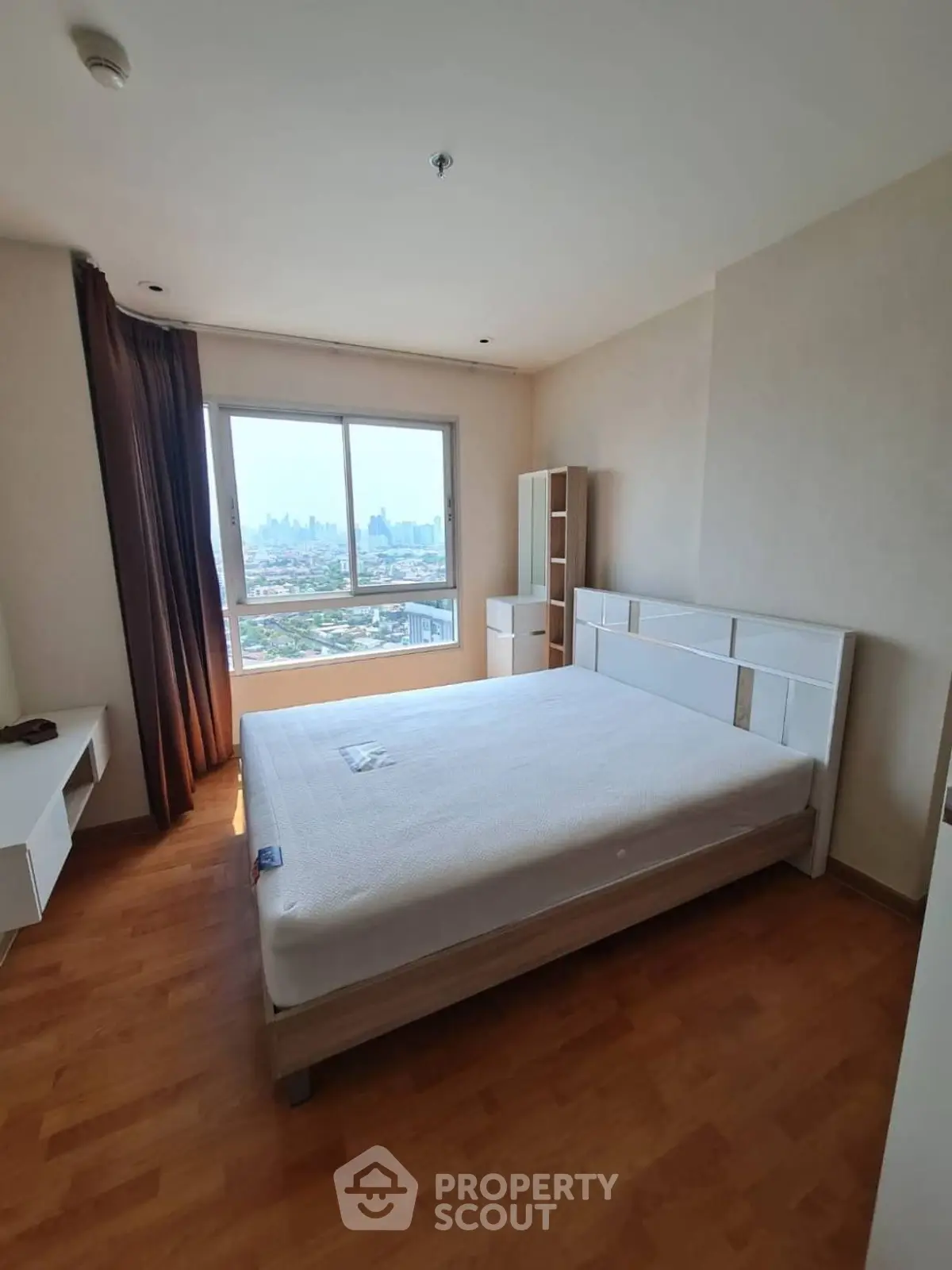 Spacious bedroom with city view and modern furnishings in high-rise apartment.
