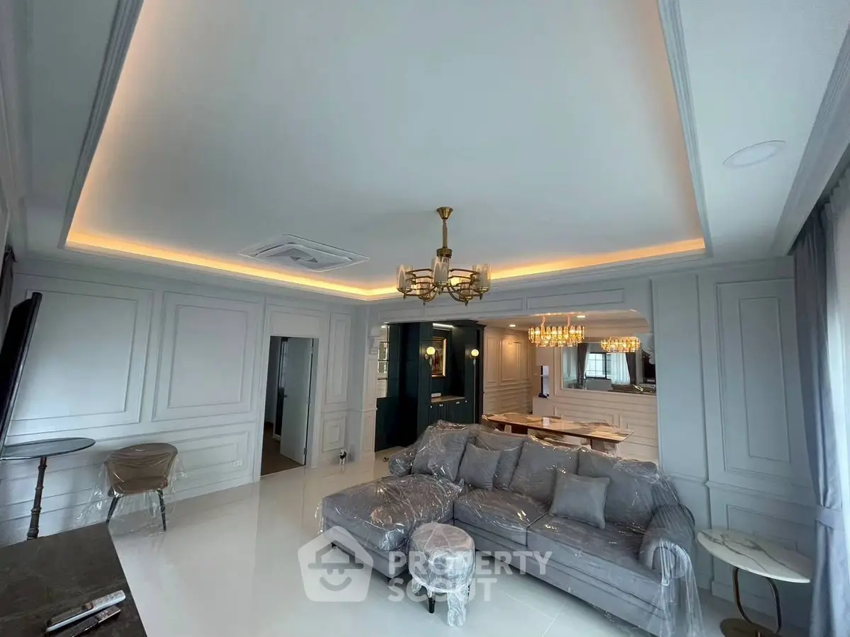 Luxurious living room with elegant chandelier and plush gray sofa in modern apartment.