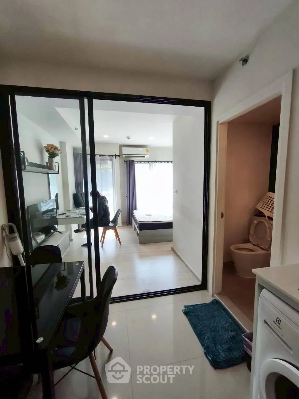Modern apartment interior with glass partition, cozy living area, and compact bathroom.