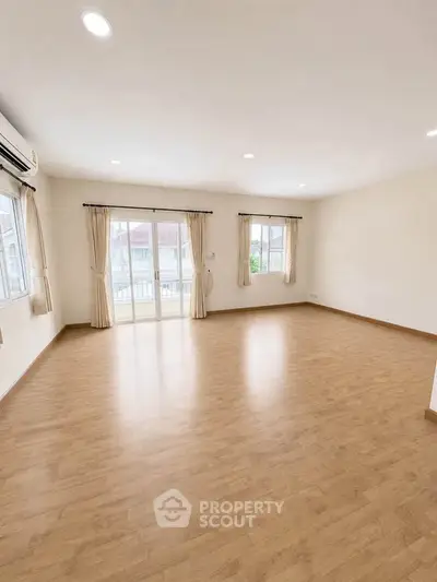 Spacious empty living room with wooden flooring and large windows for natural light.
