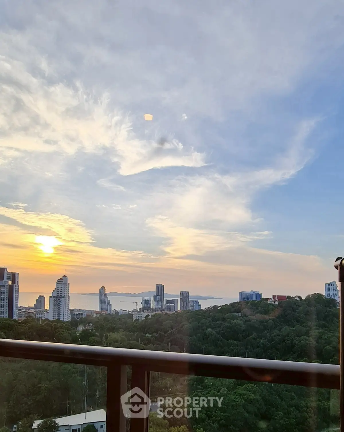 Stunning sunset view from high-rise balcony overlooking city skyline and lush greenery.