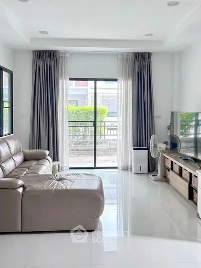 Spacious living room with modern decor and large windows offering natural light and garden view.