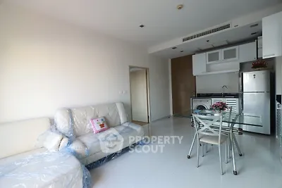 Modern open-layout living room with kitchen, featuring sleek furniture and bright natural lighting.