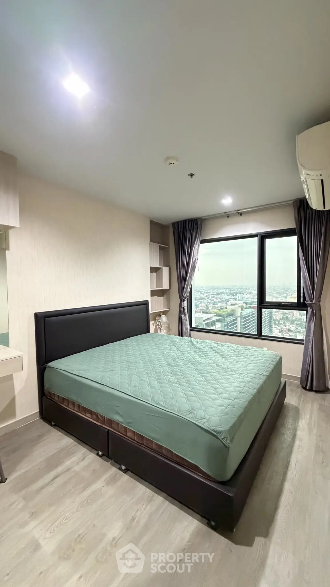 Spacious bedroom with large window offering stunning city views, modern furnishings, and elegant decor.