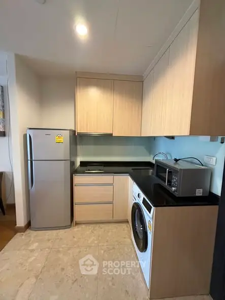 Modern kitchen with fridge, washing machine, and microwave in compact layout.