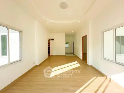 Spacious sunlit room with wooden flooring and large windows