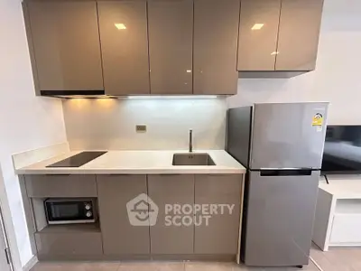 Modern kitchen with sleek cabinetry, built-in microwave, and stainless steel fridge in a compact layout.