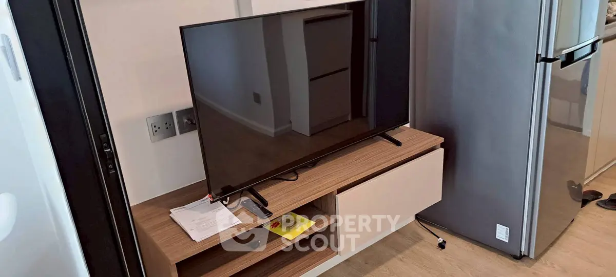 Modern living room with sleek TV unit and stainless steel fridge, showcasing contemporary design.