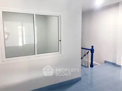 Modern interior with blue-tiled floor and white walls, featuring a window and staircase.