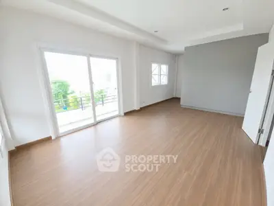 Spacious empty room with wooden flooring and large sliding glass doors leading to a balcony.