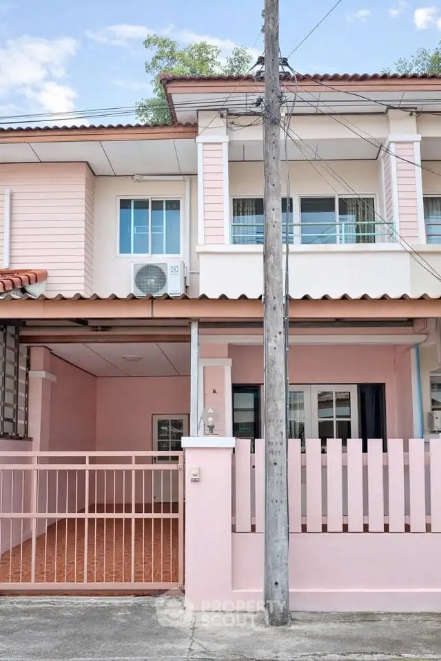 Charming pink townhouse with gated entrance and balcony in a serene neighborhood.