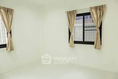 Bright empty room with tiled floor and two windows with beige curtains.