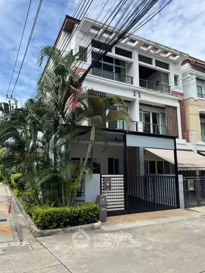 Modern three-story townhouse with lush greenery and spacious balconies in a vibrant neighborhood.
