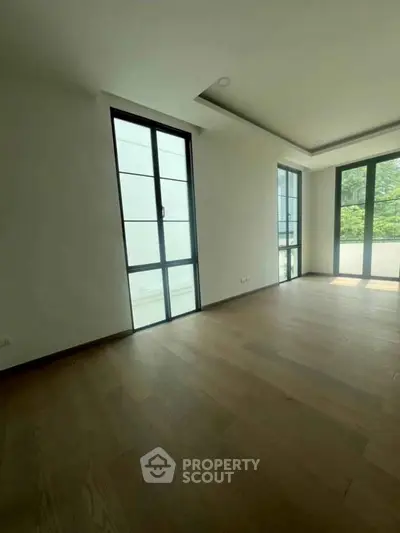 Spacious empty room with large windows and wooden flooring, perfect for customization.