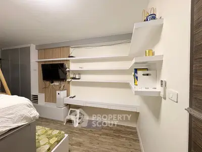 Modern bedroom with built-in shelves and wall-mounted TV, featuring stylish wood flooring and contemporary decor.
