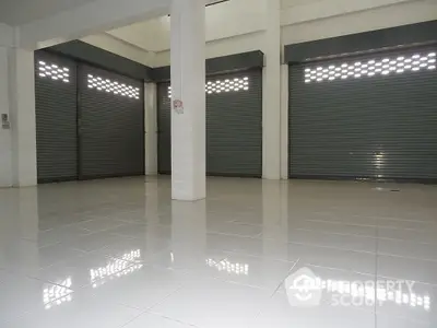 Spacious commercial space with high-gloss tiled flooring and multiple rolling shutter doors, ideal for a variety of business ventures.