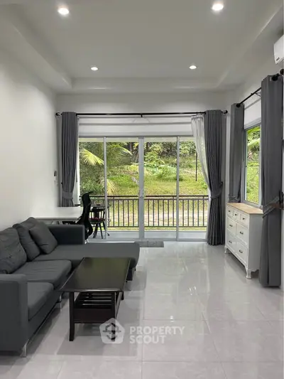 Spacious living room with modern gray sofa, large windows, and lush garden view.