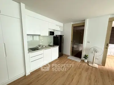 Modern kitchen with sleek white cabinets and wooden flooring in a cozy apartment.