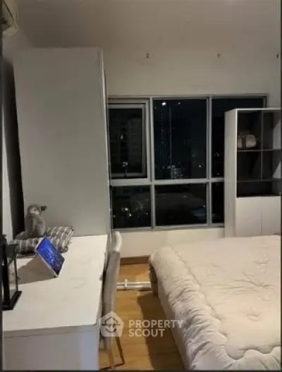 Modern bedroom with city view, featuring a cozy bed, desk, and large window for natural light.
