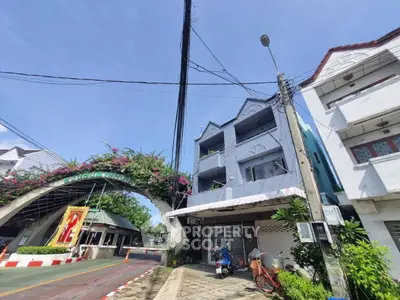 Charming three-story building with nearby archway and lush greenery, perfect for urban living.