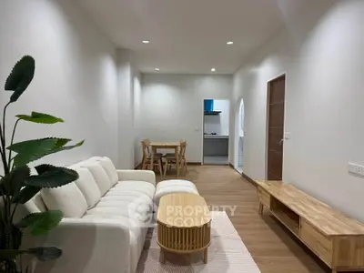 Modern living room with cozy white sofa and wooden furniture, leading to a dining area and kitchen.