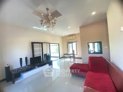 Spacious living room with modern decor and red sofa, featuring elegant chandelier and large windows.