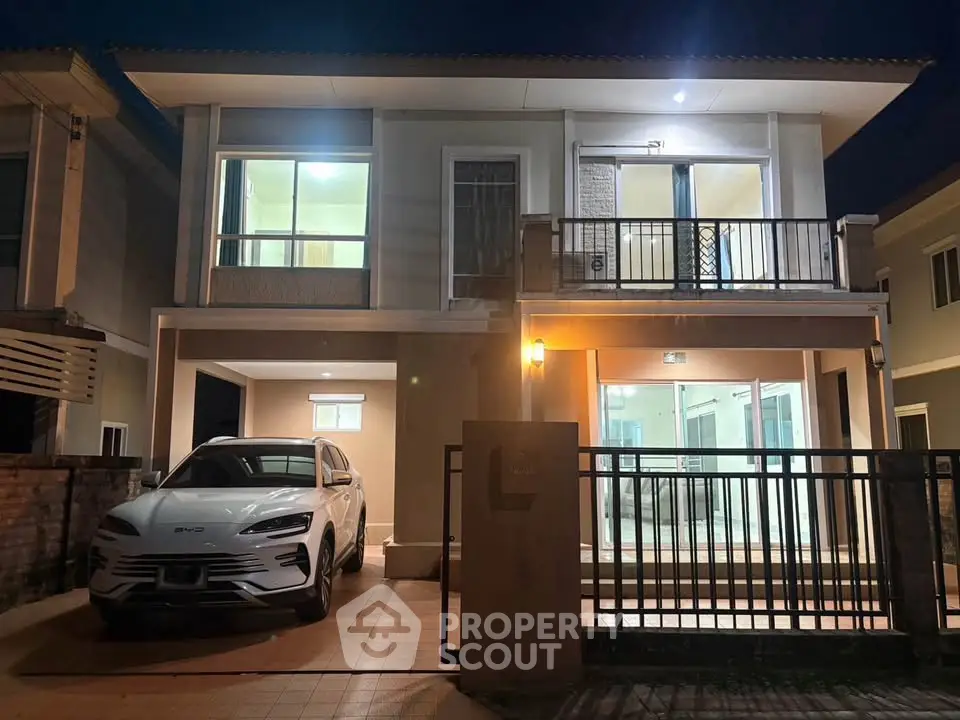 Modern two-story house with balcony and carport, featuring sleek design and illuminated interiors at night.