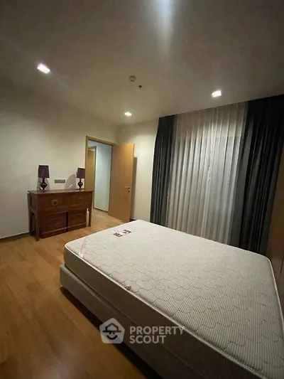Cozy bedroom with wooden flooring and elegant curtains, featuring a comfortable bed and stylish furniture.